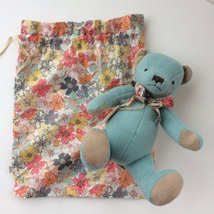 Beautiful Blue Teddy Bear - A timeless gift This beautiful blue teddy bear arrives in a floral cloth bag with a matching floral bow tie around his neck. This classic high quality teddy bear is timeless and will be treasured for years to come. Made with soft velour light blue fabric, he has acrylic bead eyes and an embroidered nose and mouth. Showing bear and floral bag which the bear arrives in.